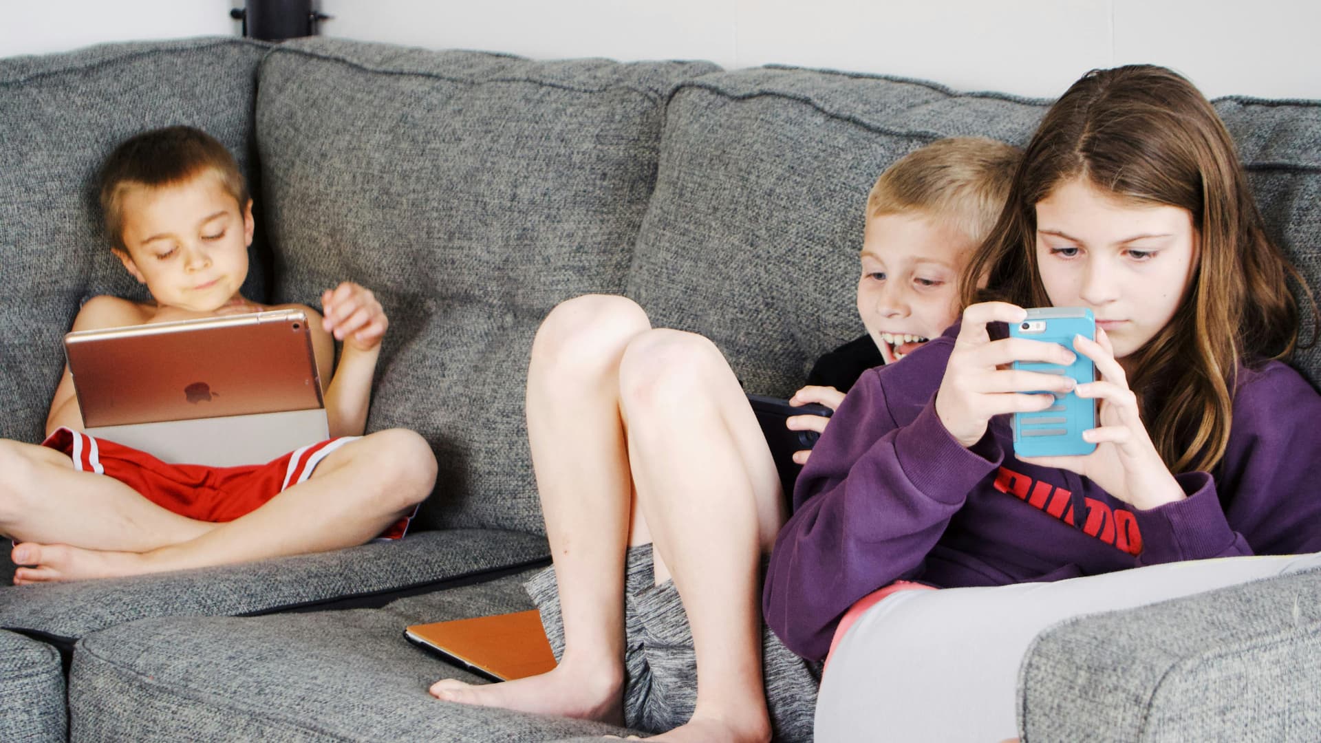 Drei Kinder sitzen auf einem Sofa und benutzen iPhone und iPad