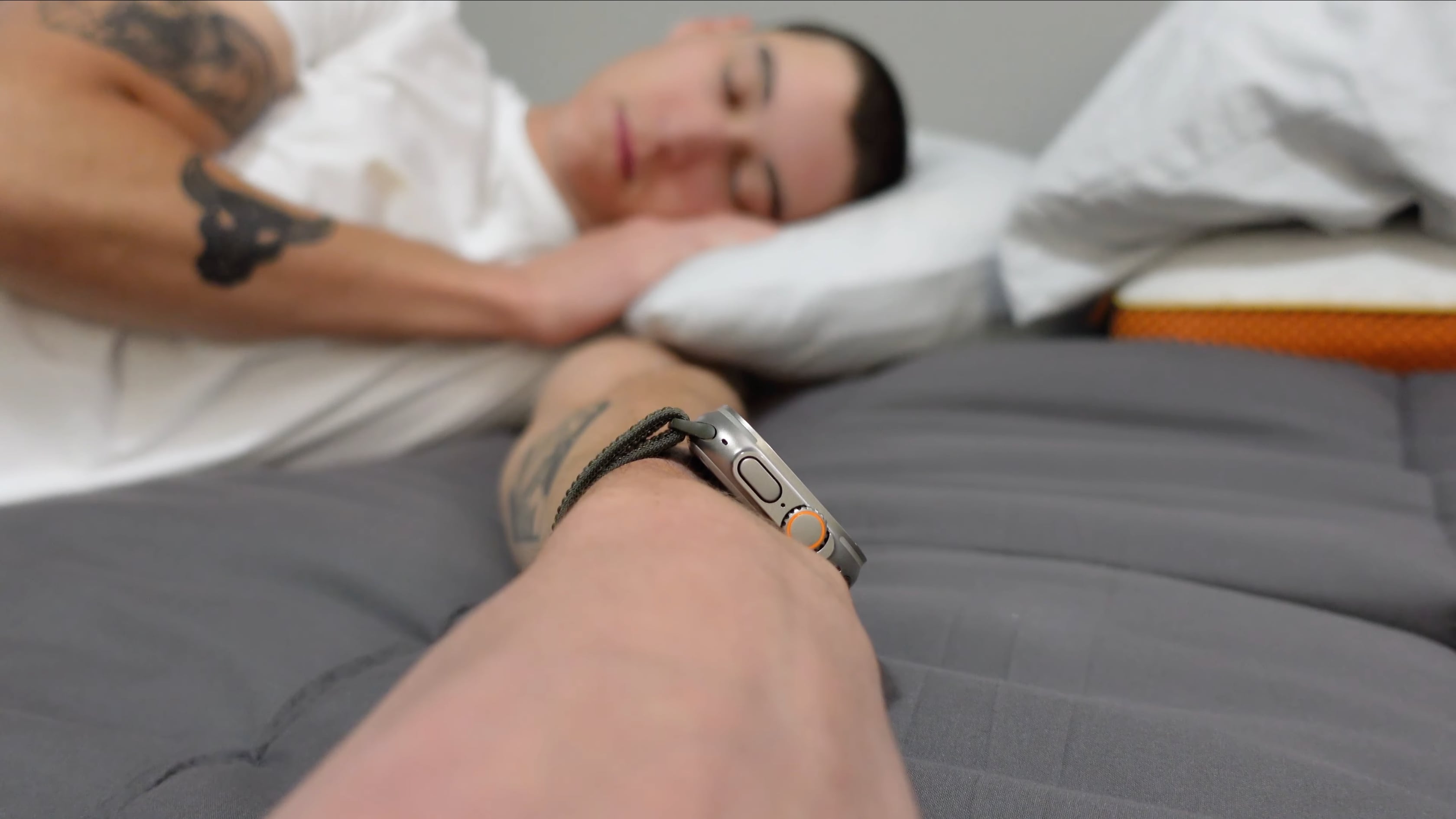 Ein junger Mann schläft in seinem Bett und trägt eine Apple Watch Ultra am Handgelenk