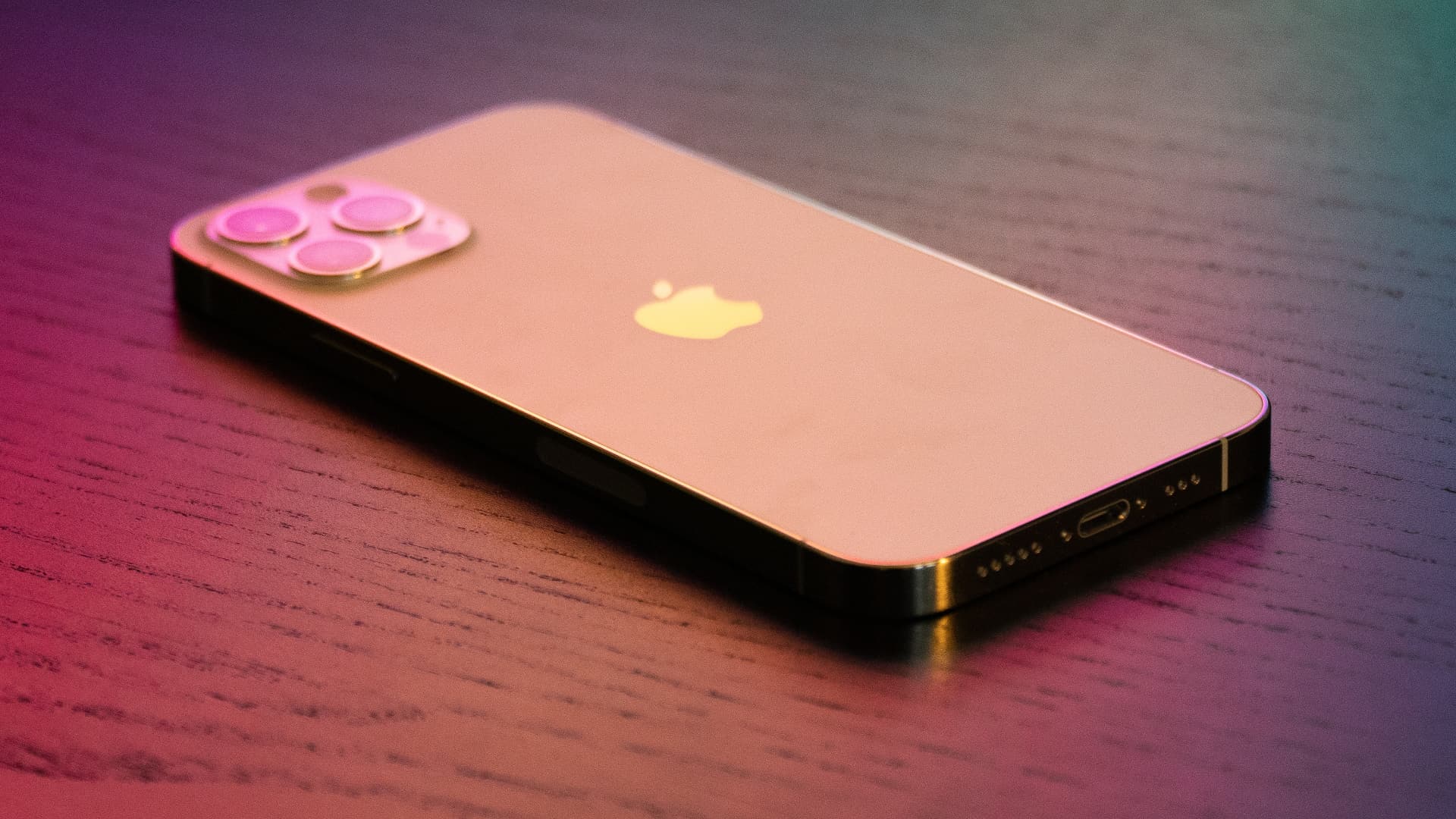 Gold iPhone 12 Pro unter farbenfrohen Beleuchtung, Facedown auf einem Holztisch gesetzt