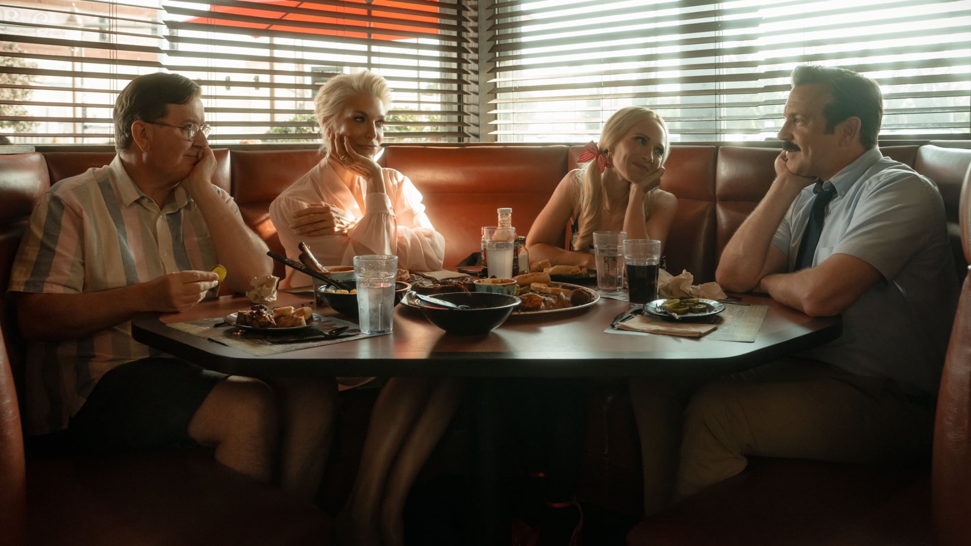 Eine Szene aus Ted Lasso Staffel 4, mit dem Trainer und anderen Charakteren um einen Restauranttisch versammelt.