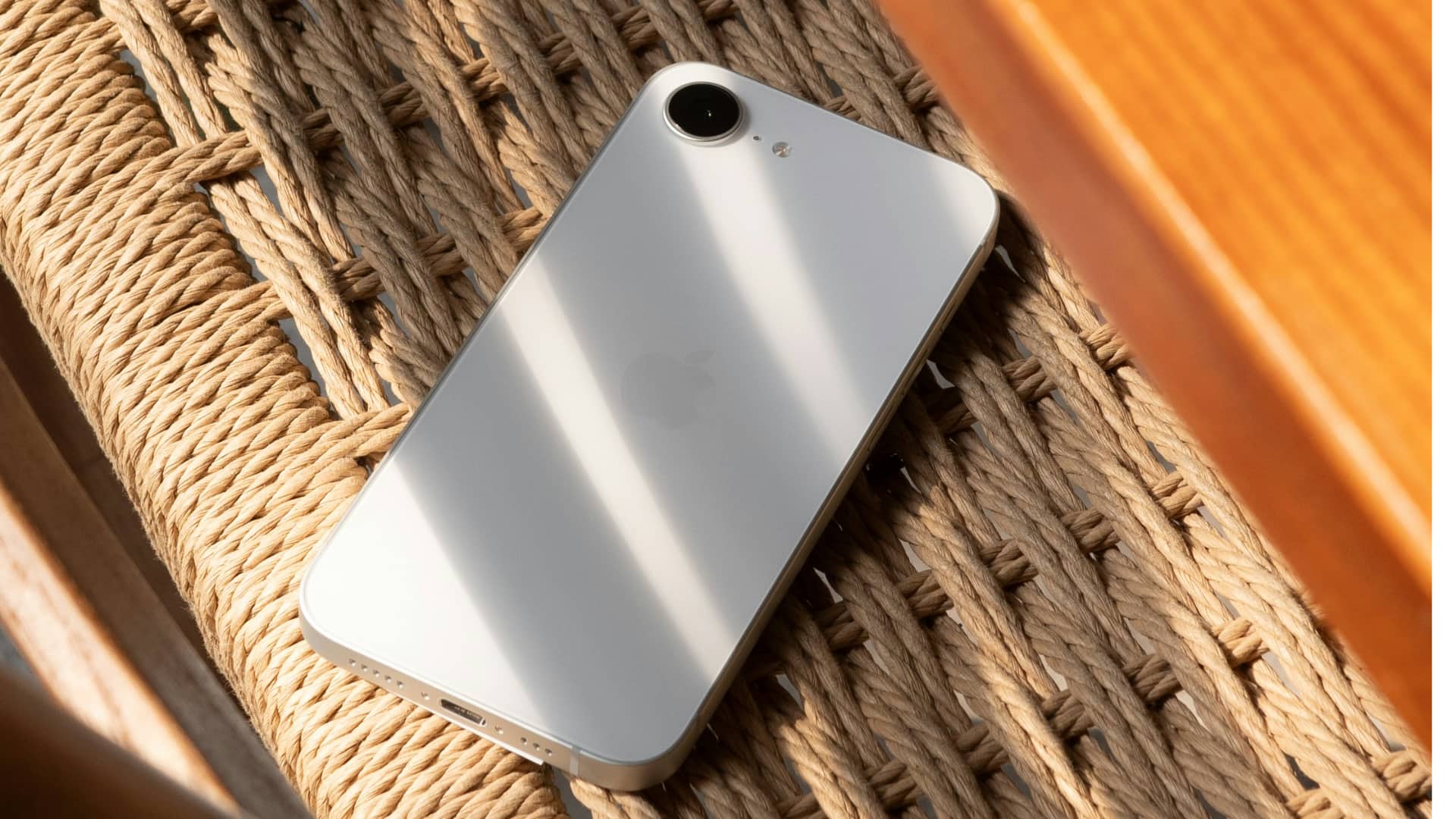 Top-Down-Ansicht eines weißen iPhone 16E-Gesichtstarts auf einem Whicker-Stuhl